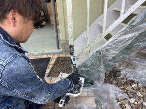 滋賀県大津市で戸建て住宅の鉄骨階段塗装、古い塗膜を剥離させるためのリムーバー剤を職人が刷毛で下から１段目の手摺りの柱に塗布している様子